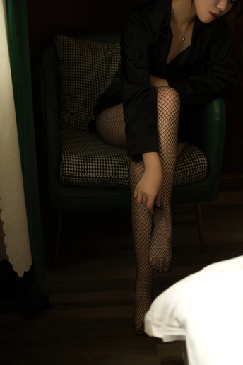 一个穿着黑色连衣裙和紧身裤的年轻女子坐在椅子上