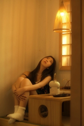 一个年轻女子坐在一个被灯照亮的房间里的一张桌子上。
