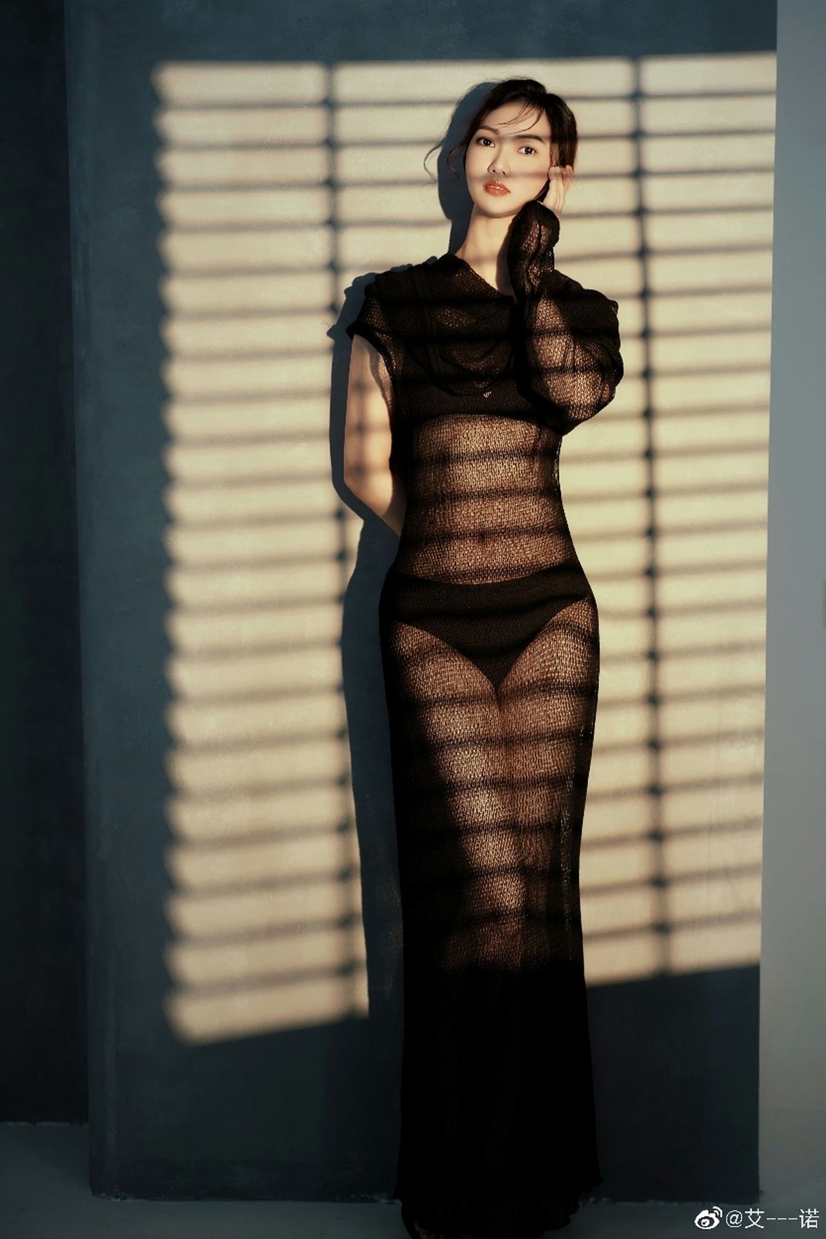 一位穿着黑色连衣裙的女人站在窗前 墙上有些阴影。