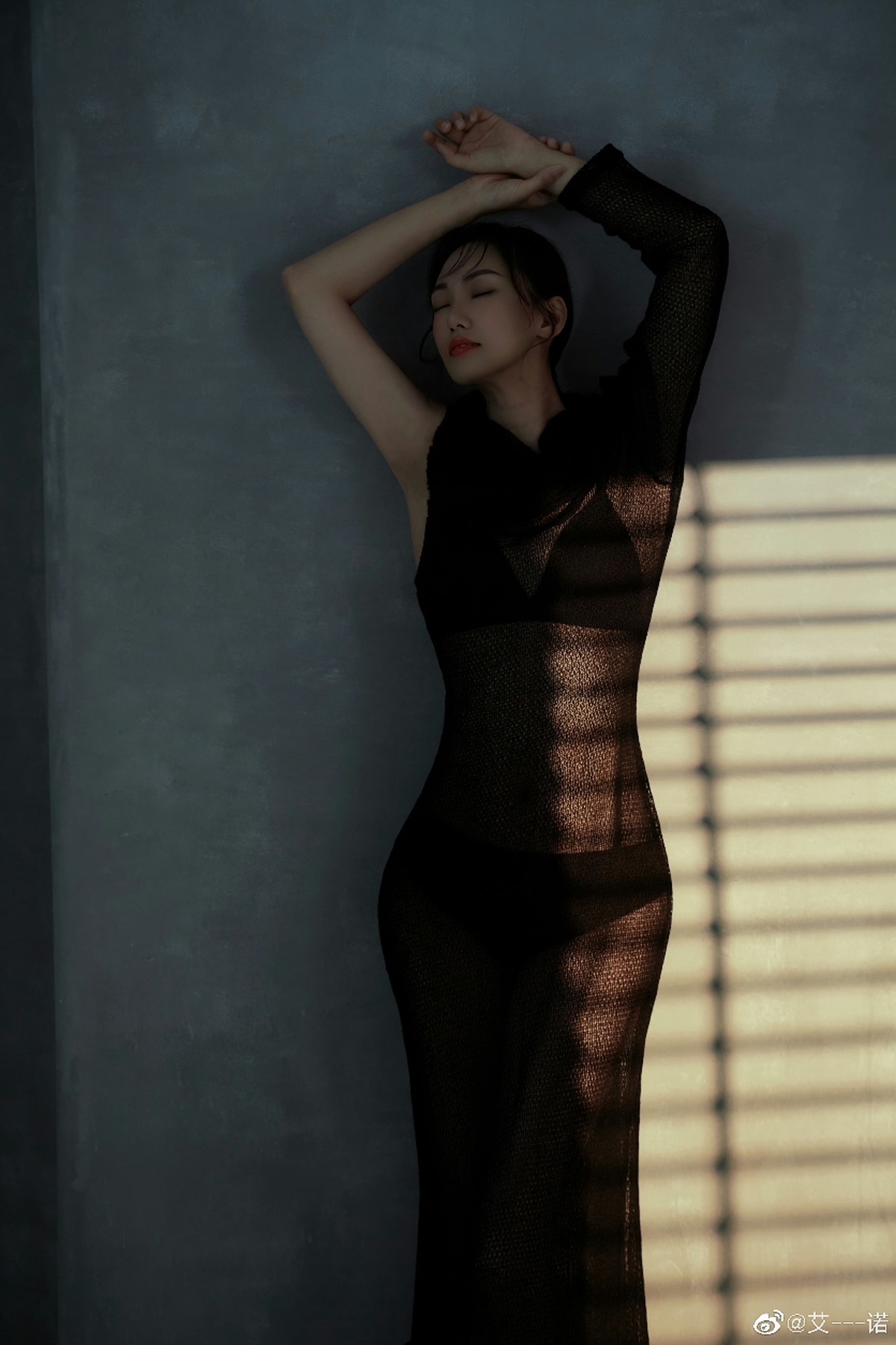 一位穿着黑色连衣裙的年轻女子站在窗前 在墙上投下阴影。
