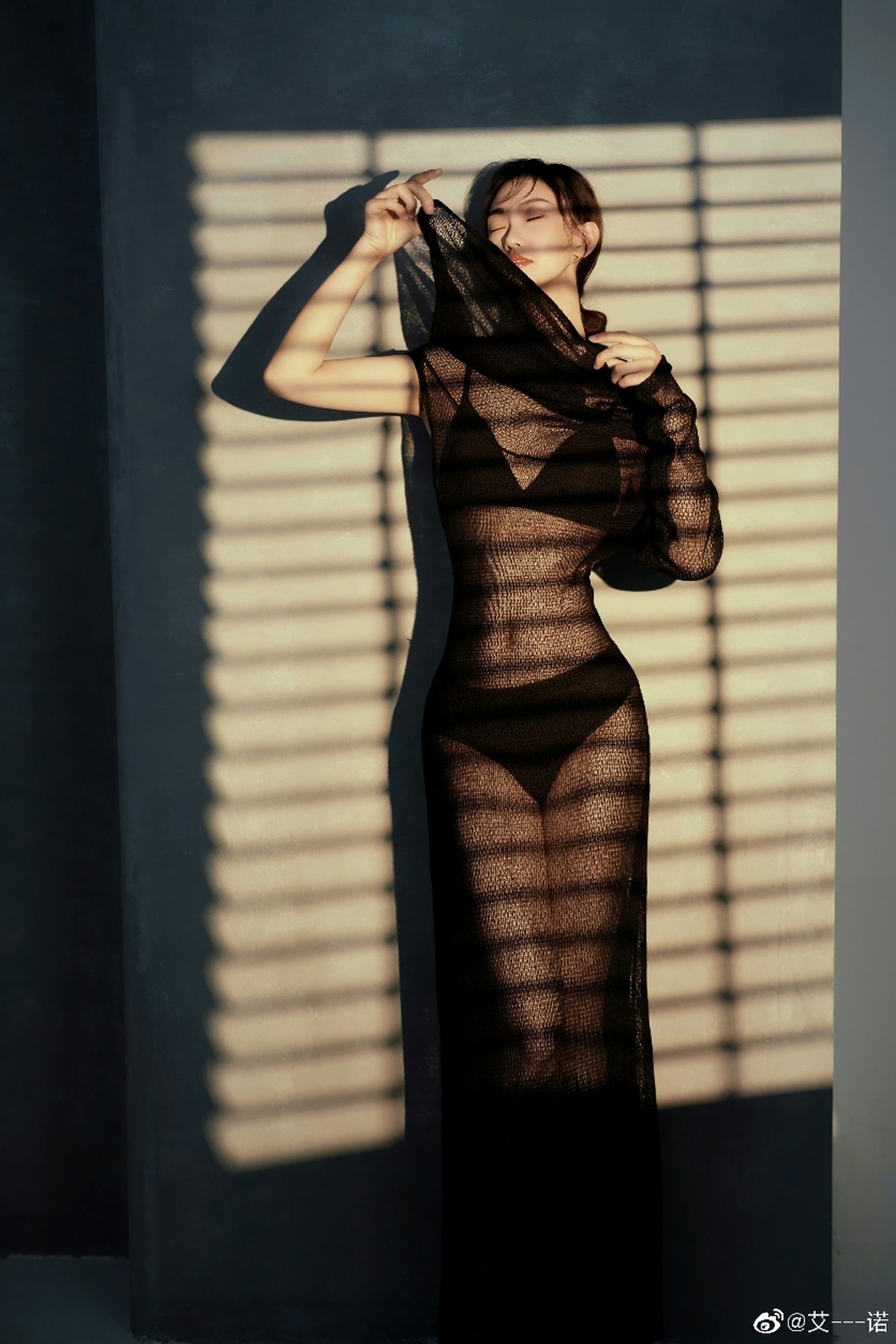 一位穿着黑色连衣裙的女人站在窗前 墙上有些阴影。