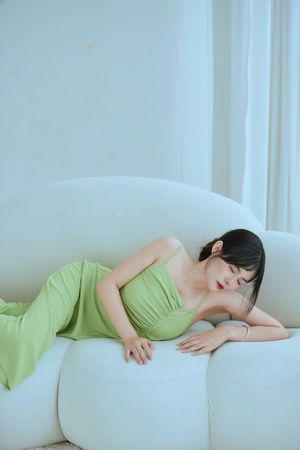 一个穿着绿色连衣裙的年轻女子躺在白色沙发上