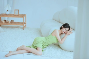 一个年轻美丽的穿着绿色连衣裙的女子躺在白色的房间里 旁边有一把白色的椅子。