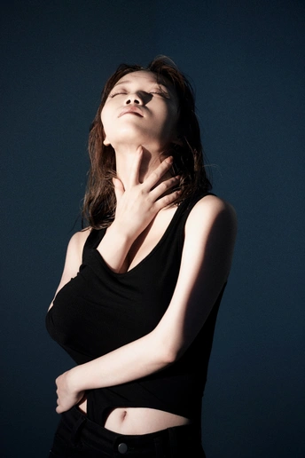一位年轻女子穿着黑色上衣在深色背景前摆姿势