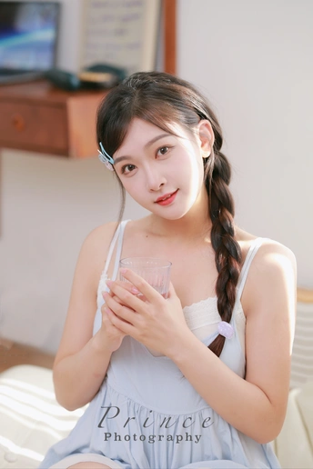 一个年轻女子坐在床上 手里拿着一杯水和吸管。