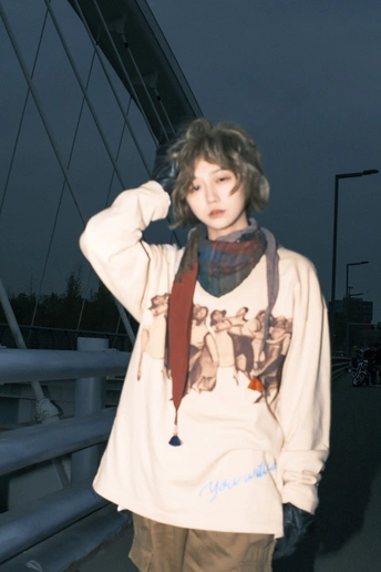 一位穿着运动衫的年轻女子站在滑板上在桥上