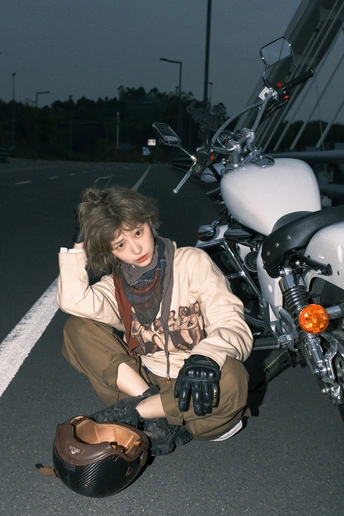 一位年轻女子坐在路边 旁边有一辆白色摩托车 正在为拍照姿势 