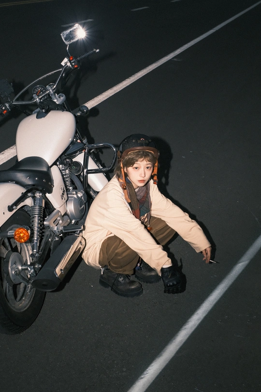 一个戴头盔的年轻女子坐在白色摩托车上 停在停车场。