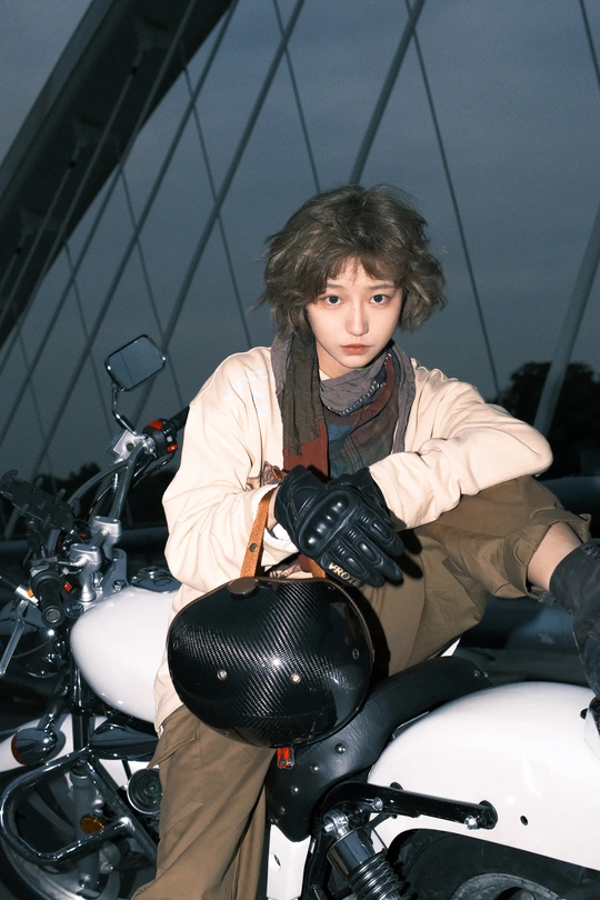 一个戴头盔和手套的年轻人坐在白色摩托车上 背景中有桥。