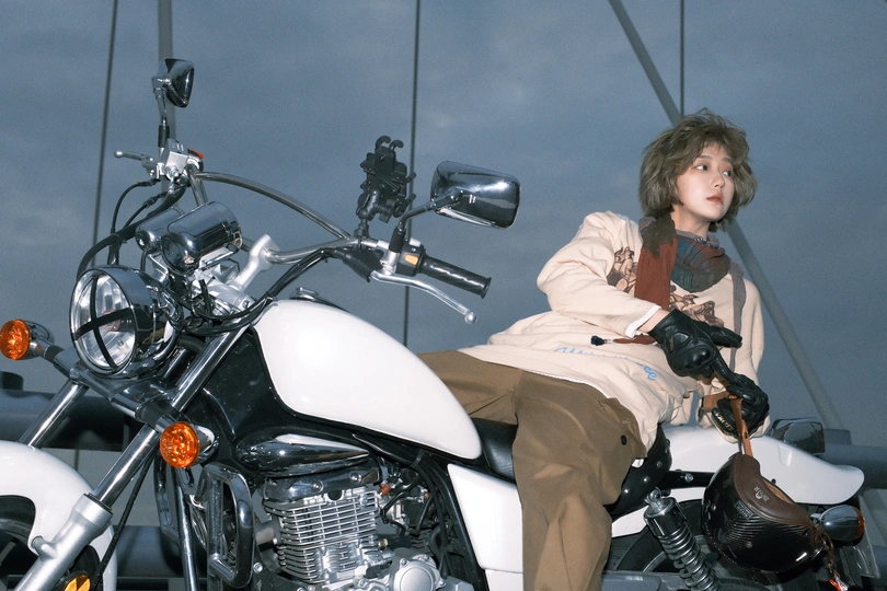 一位年轻女子坐在白色摩托车上 背景中一位男子在摆姿势。