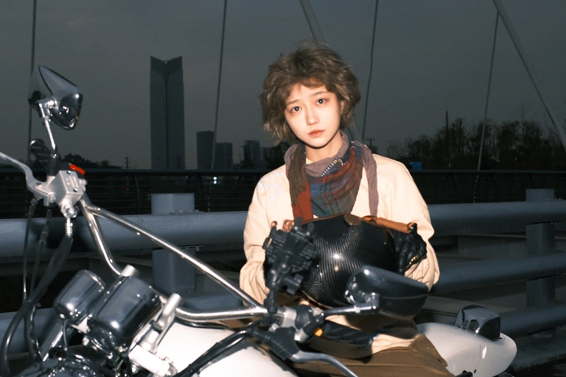 一位年轻女子坐在摩托车上 一位男子站在她身后的一座桥上。