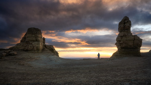 一个人站在沙漠中 天空中是夕阳 背景是岩石地貌