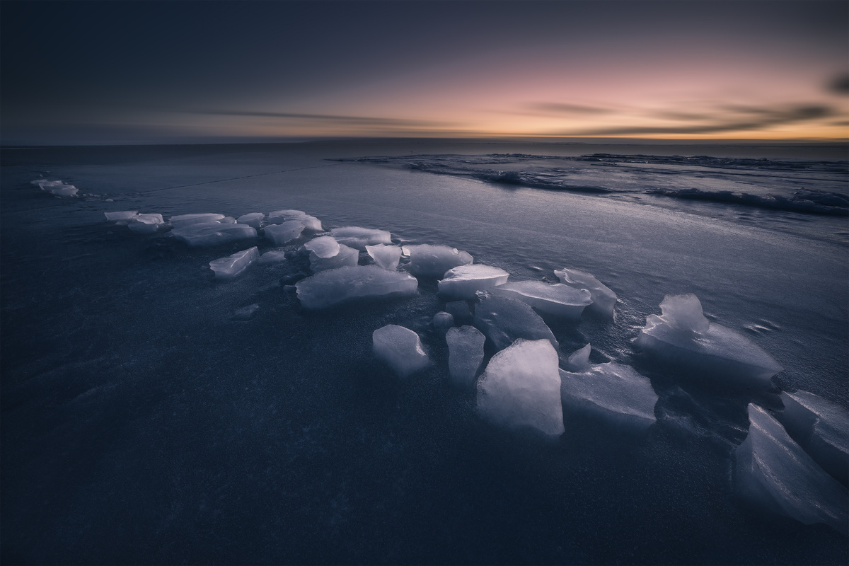 夕阳下冻结的海滩上有冰山在水中和天空中。