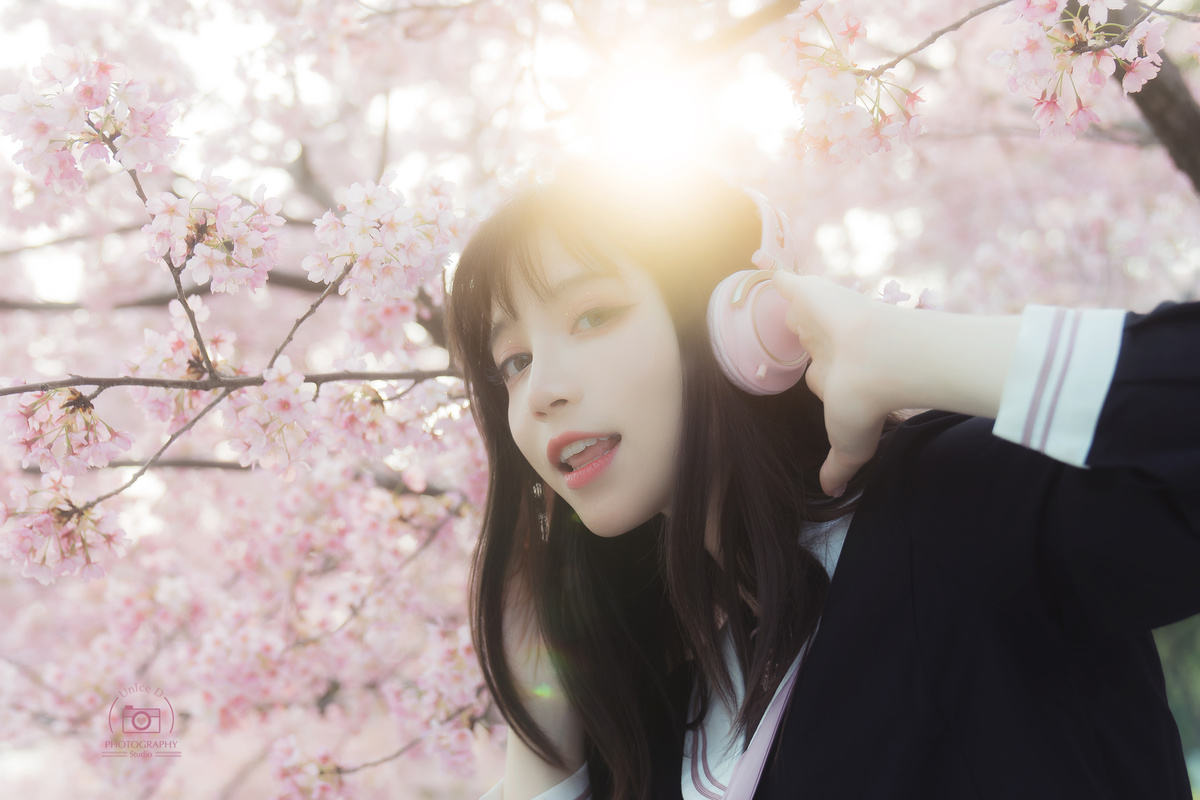 阳光下 一位年轻女子站在开着粉红色花朵的樱桃树下