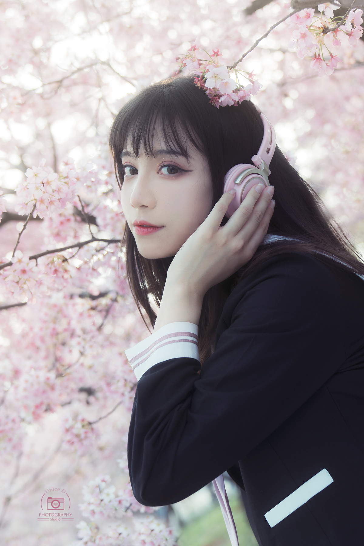 一位年轻女子站在一棵开着粉红色花朵的树下 把手机放在耳边