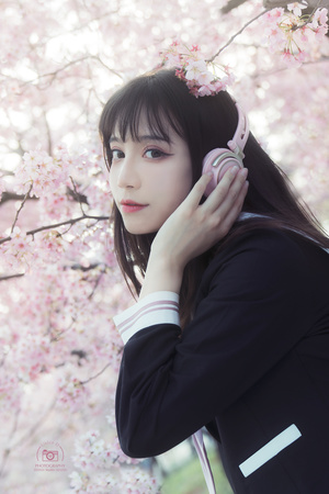 一位年轻女子站在一棵开着粉红色花朵的树下 把手机放在耳边