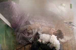 一个穿着连衣裙的年轻女子躺在地板上 旁边有白色的花。