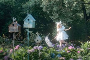 一个小女孩穿着一件白色连衣裙在花园区中与鸟儿一起奔跑