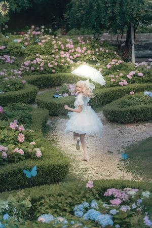 一位穿着白色连衣裙的小女孩在花园区的小径上奔跑 手里拿着一把雨伞。