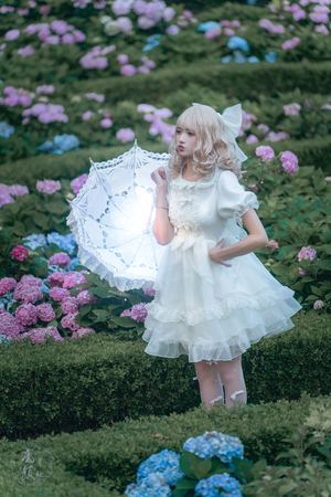 一个穿着天使装的年轻女孩 带着白色的翅膀和一把雨伞 在开满鲜花的花园里 有一片花的田野。
