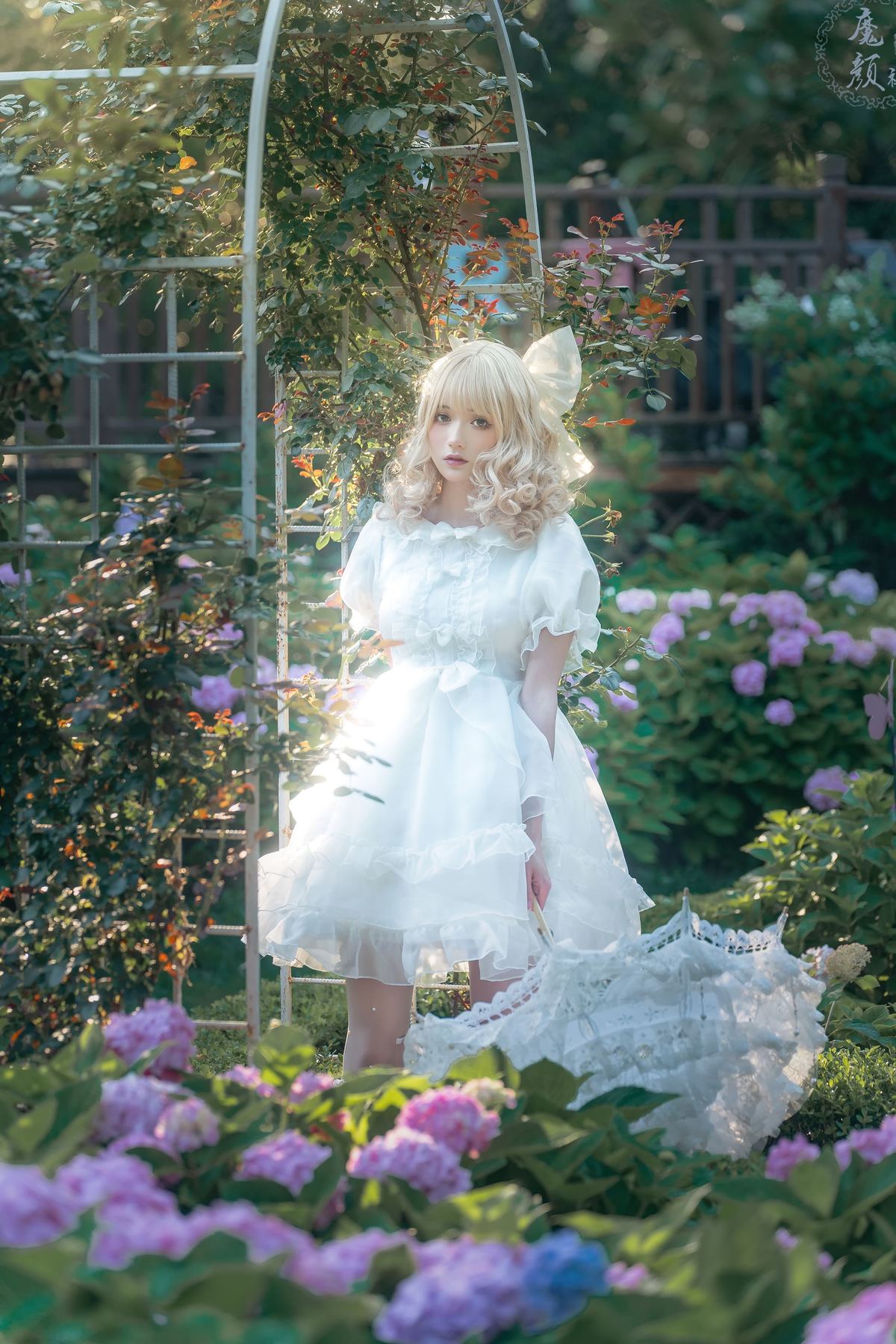 一个小女孩穿着一件白色连衣裙站在一个秋千上 在一个花坛中。