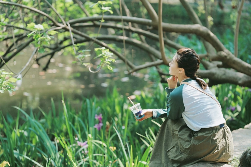 一位年轻女子坐在树下在花园里河边的画