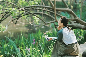 一位年轻女子坐在树下在花园里河边的画