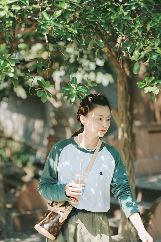 一位穿着传统服装的年轻女子手持一杯饮料站在一棵树下。