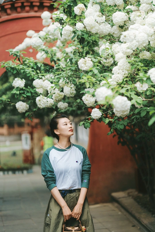 一位穿着裙子的年轻女子站在一棵开满白色花朵的树前