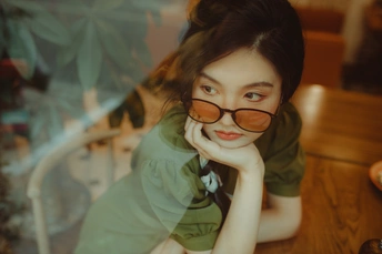 一个戴眼镜的年轻女子坐在桌子旁 身着一件绿色衬衫。