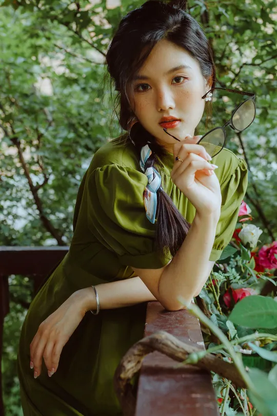 一位穿着绿色连衣裙的女子正在花旁边摆姿势