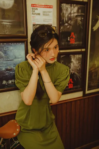 一位穿着绿色连衣裙的年轻女子站在一面墙前