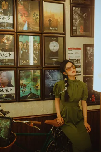 一位戴眼镜的女士穿着绿色连衣裙在贴满海报的房间里摆姿势