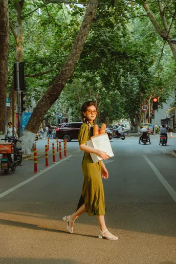 一位穿着绿色连衣裙的年轻女子拿着一张纸在一条栽满树街道上走下来