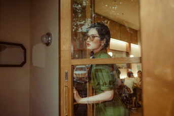 一位穿着绿色连衣裙的女士站在一扇玻璃门后面的一间房间里