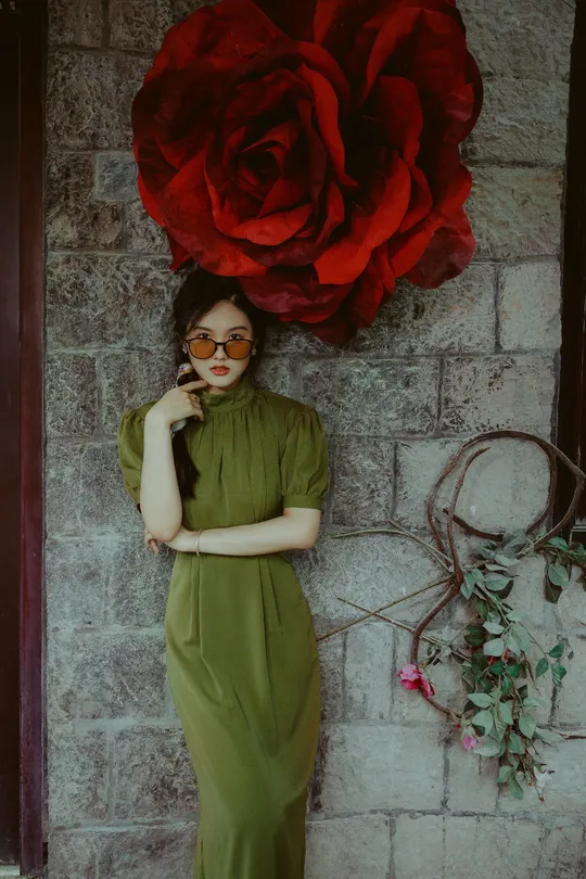 一位穿着绿色连衣裙的女人站在一个有红花的墙壁前