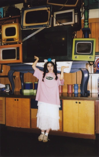 一个穿着连衣裙的小女孩举起双手 above her head 在一个堆满杂物 的房间里