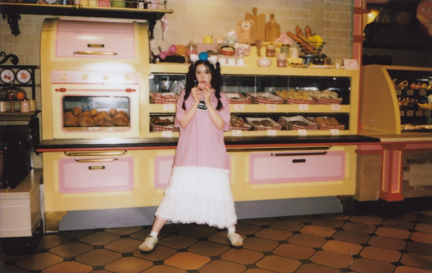 一位穿着粉红色连衣裙的年轻女子在商店厨房里为拍照做姿势