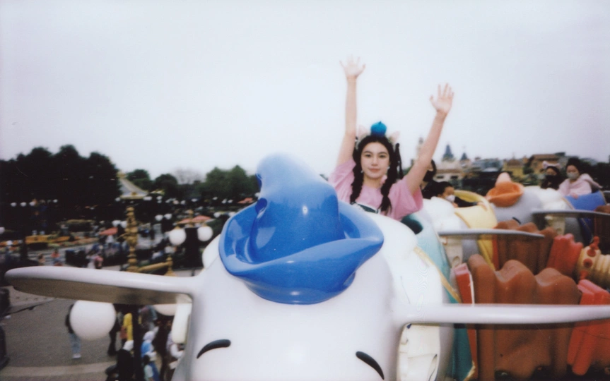 一个小女孩在游乐园里骑着小型飞机挥手。