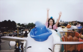 一个小女孩在游乐园里骑着小型飞机挥手。