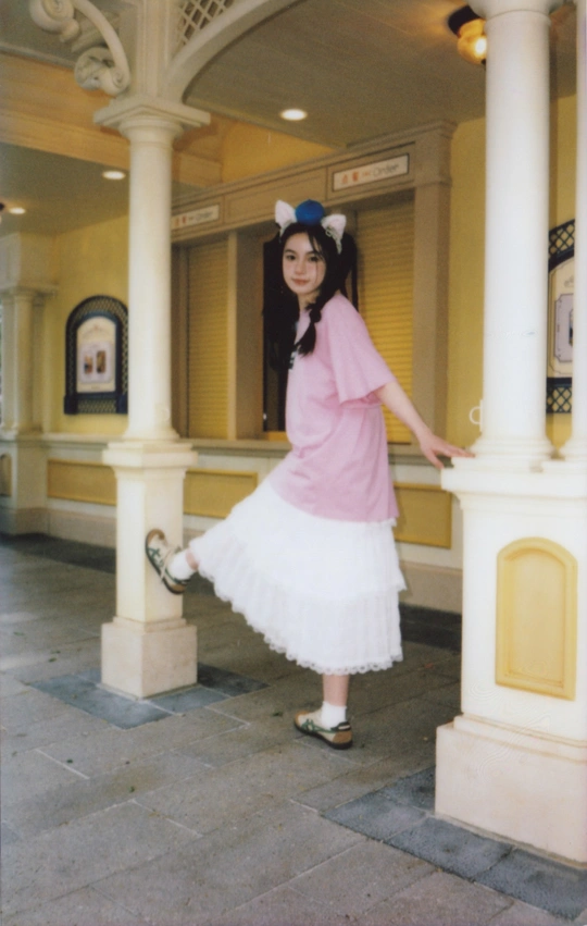 一位穿着粉红色连衣裙的年轻女子站在一白色柱子旁边