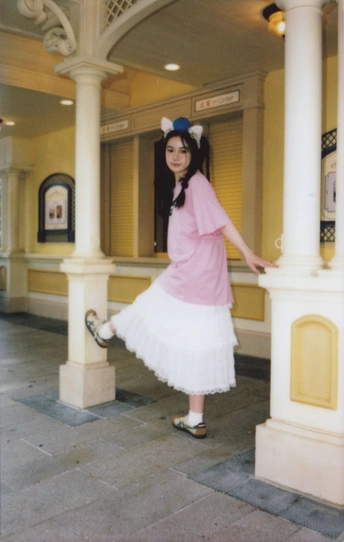 一位穿着粉红色连衣裙的年轻女子站在一白色柱子旁边