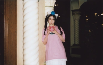 一个小女孩穿着粉红色裙子 手里拿着一个杯子 站在一个柱子旁边。