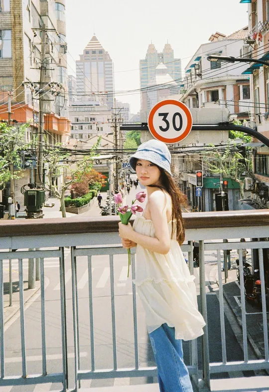 戴帽子的一位年轻女子站在街头 手里拿着花。