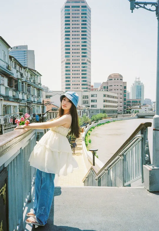 一位穿着白色连衣裙和蓝色帽子的年轻女子在河上的桥上摆姿势
