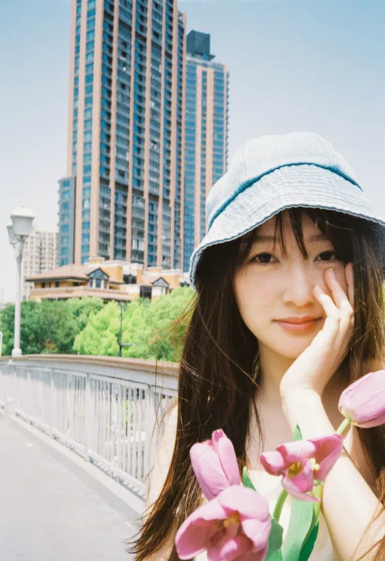 一位穿着蓝色帽子 拿着粉色花朵站在桥上的年轻女子