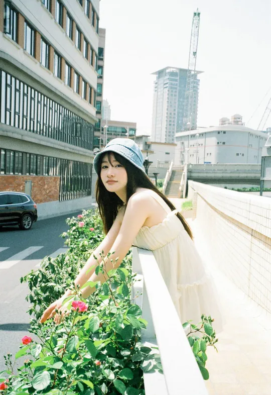 一位穿着连衣裙和帽子站在街上的桥上的年轻女子