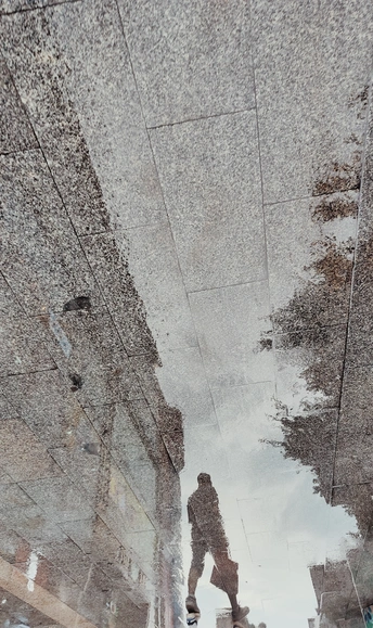 街上一个撑着雨伞的男人在水坑里行走的倒影