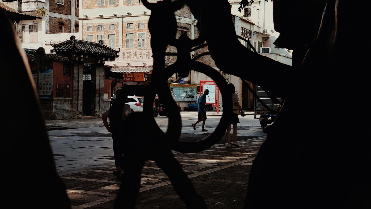 背景是建筑物的街道上 一个人撑着伞站在自行车旁边的剪影