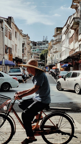 一个戴草帽的男人骑着自行车沿街而行